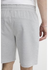 Shorts de sport gris clair en tissu doux, dotés d'une taille élastique et d'une surface texturée. Pas de poches visibles ni de motifs.