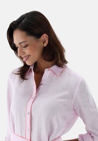 Camicia di lino rosa chiaro con colletto button-down e rifiniture arancioni a contrasto. Presenta una vestibilità morbida e una texture liscia.