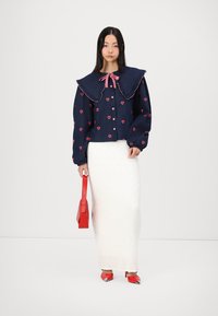 Ναυτικό τζάκετ τζιν με κόκκινες καρδιές, υπερμεγέθη ρυτιδωτό γιακά, δεμένο φιόγκο, σε συνδυασμό με λευκή υφασμάτινη φούστα, κόκκινη τσάντα και παπούτσια.