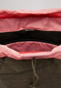 Interior de mochila con forro a rayas rojas y blancas y compartimento acolchado negro para portátil etiquetado "Bienvenido a Herschel".