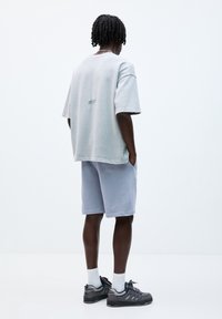 T-shirt surdimensionné gris clair avec un design minimaliste, associé à un short bleu pâle. Baskets noires avec des accents gris et des chaussettes blanches.