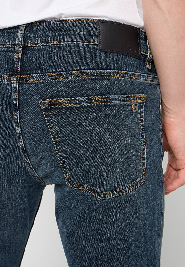 Jean en denim bleu foncé au design classique, doté de poches arrière, de coutures contrastantes et d'une étiquette de marque en cuir noir à la taille.