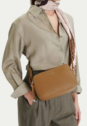 Kobieta w beżowej jedwabnej bluzce i apaszce, niosąca beżową skórzaną torebkę na ramię z przeszywanymi krawędziami i logo LASOCKI.