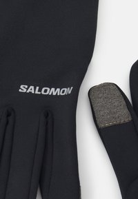 Čierne rukavice s textúrovaným uchopením na prstoch. Na zápästí sa nachádza sivé logo "SALOMON". Hladká tkanina s priliehavým strihom.