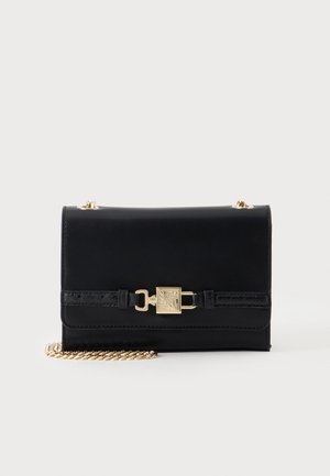 Sac bandoulière en cuir noir avec bandoulière chaîne dorée et fermoir carré doré sur le rabat avant, sur un fond clair uni.