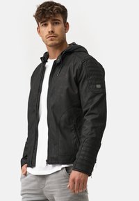 Schwarze Lederjacke mit Kapuze, versehen mit gesteppten Schulter- und Armdetails, Reißverschluss-Taschen und tailliertem Design. Weiße Innenschicht sichtbar.