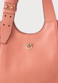 Torba od koraljno ružičaste kože s podesivim remenom, detaljno prošivena, s zlatnim dvostrukim grbom ptice na središnjem dijelu.