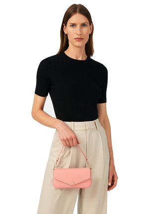 Donna che indossa un top corto a righe nero e pantaloni beige a vita alta, mentre tiene una piccola borsa rosa per la tracolla con una mano.