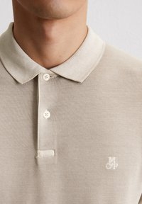 Jasno beżowa koszulka polo z teksturowanej tkaniny. Posiada klasyczny kołnierzyk, dwa guziki oraz haftowane logo "MOP" w kolorze białym.