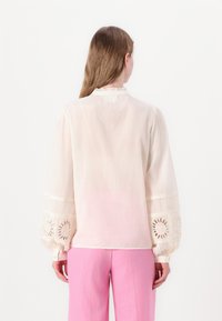 Light cream blouse with long, puffed sleeves featuring intricate lace embroidery. Slightly sheer fabric with a delicate collar and simple buttons.