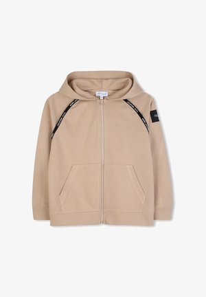 Sweat à capuche beige zippé avec poches avant, bordure diagonale noire avec texte blanc, poignets côtelés et un patch noir sur la manche gauche.