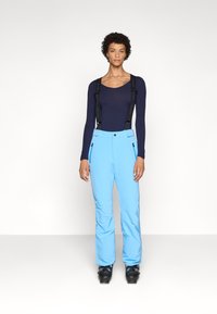 Lichtblauwe skibroek met verstelbare zwarte bretels, voorzakken met rits en een zachte textuur, gecombineerd met een marineblauw langetermijn shirt.