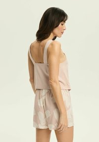 Jasnoróżowa bezrękawnik z kwadratowym tyłem i szerokimi ramiączkami, w zestawieniu z szortami wzorzystymi w podobnym kolorze. Gładka tekstura na całej powierzchni.