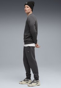 Grauer Pullover und passende Jogginghose, schwarze Mütze und beige Sneakers. Glatter Stoff mit einem Logopatch auf der Jogginghose. Lässige Passform.