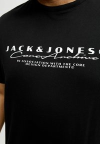 Czarny bawełniany T-shirt z białym nadrukiem: "JACK & JONES Core Archive" oraz "W SPÓŁPRACY Z DZIAŁEM PROJEKTOWYM CORE."