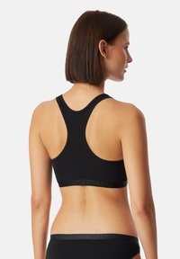 Zwarte sportbeha met een racerbackontwerp, gemaakt van zacht materiaal, met een brede elastische band met subtiele branding aan de onderkant.