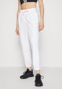 Vita idrottsbyxor med elastisk midja och dragsko. Har smalnande mudd. Kombination med svarta idrottsskor.