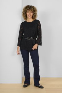 Black lace top with three-quarter sleeves and scalloped hem, paired with dark blue flared jeans and black loafers. Simple belt accent.