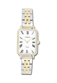 Montre rectangulaire avec un bracelet en métal argenté et doré, un cadran blanc, des chiffres romains noirs et une petite étiquette "Vintage".