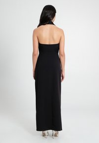 Schwarzes, ärmelloses Halterkleid mit tailliertem Oberteil und fließendem Rock. Glattes Material mit einem klaren Linien-Design. Durchscheinende Absätze sind sichtbar.