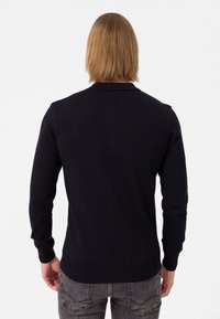 Pull en tricot noir à manches longues, avec des bords côtes aux poignets et à l'ourlet. Design simple, texture lisse, sans motifs ni accents visibles.