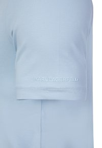 Lyseblå kortærmet t-shirt med prægede "KARL LAGERFELD" logo nær den nederste kant af ærmet.