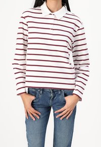 Camisa de polo blanca de manga larga con rayas horizontales en color burdeos, con un cuello clásico y una tapeta de botones. Combinada con jeans azules.