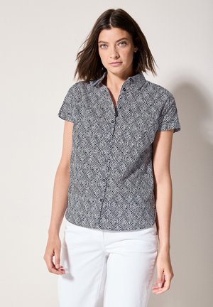 Short-sleeve shirt in black and white, featuring a leaf pattern, collared neckline, and a button front. Fabric appears lightweight and textured.
