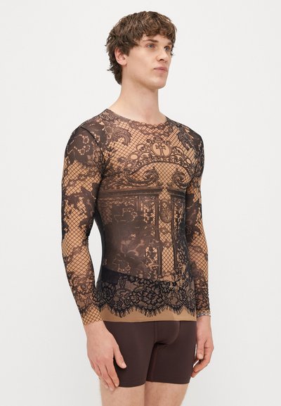 Top in pizzo nero a maniche lunghe con intricati motivi floreali su uno strato di base nudo; abbinato a pantaloni corti marroni aderenti. Design testurizzato su tutta la superficie.