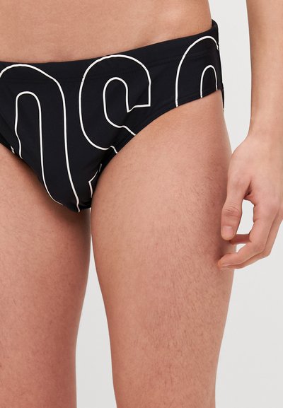 Maillots de bain noirs avec un design en lettres blanches, présentant une texture lisse et une coupe ajustée, conçus pour le confort et la mobilité.