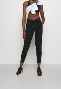 Svarta atletiska joggers med dragsko i midjan, resår i bensluten och logotypdetalj. Matchas med en svart crop top och en vit sweatshirt knuten runt midjan.