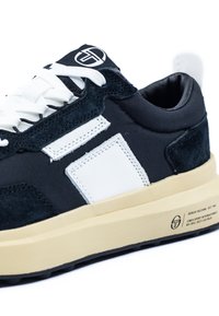 Schwarze Wildleder- und Nylon-Sneaker mit weißen Lederakzenten, flachen weißen Schnürsenkeln und einer beigen Gummisohle. Besitzt ein Logo auf der Zunge.
