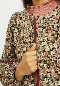 Blommönstrad jacka i svart, rosa och vitt, med en smockad krage och knappstängning. Texturerat tyg med rynkade ärmar.