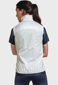 Veste légère sans manches en blanc et marine. Caractéristiques : col montant, ourlet élastique et matériau lisse et résistant à l'eau.