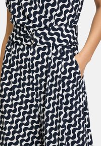 Marinblå och vit mönstrad byxdress med en vågig design, en bälte midja med en cirkulär spänne, och sidofickor. Tillverkad av ett lätt tyg.