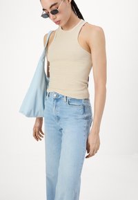 Svetlobéžová rebrovaná tank top s tenkými ramienkami, kombinovaná so svetlomodrými vysokými džínsami a mäkkou modrou tašky. Tmavé slnečné okuliare dopĺňajú celkový vzhľad.