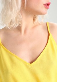 Top sin mangas amarillo con diseño de escote en V, hecho de tela texturizada, con tirantes finos y un corte relajado.