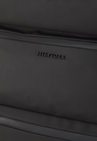 Black nylon backpack featuring a smooth texture, minimalistic design, and embossed "HILFIGER" logo on the front panel.