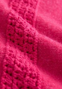 Țesătură tricotată roz aprins cu un model texturat croșetat și secțiuni netede. Moale, cu o ușoară pufozitate și grosimi variate.