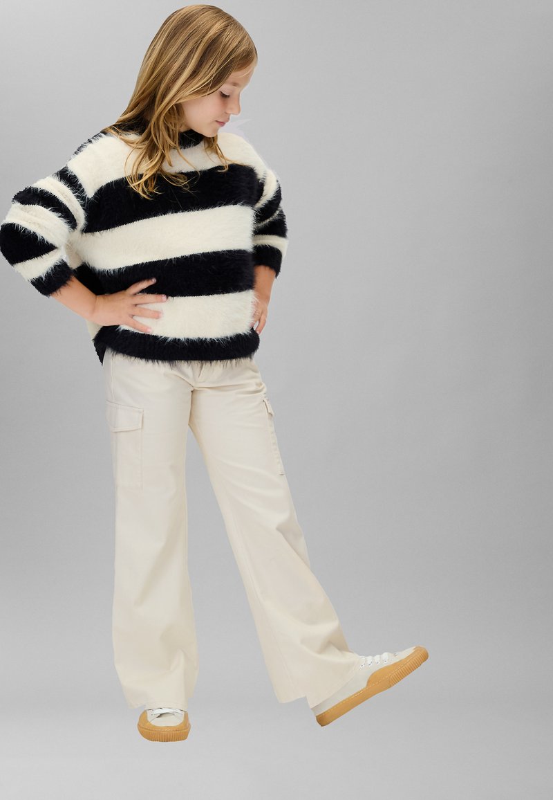 Pull duveteux à rayures noires et blanches, pantalon cargo beige à jambes larges, et baskets blanches à semelle gomme, mettant en valeur une coupe décontractée et une texture.