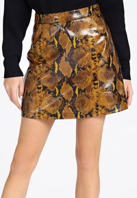 Mini gonna lucida con motivo di pelle di serpente marrone e nera, indossata con una maglietta nera a maniche lunghe, mostrata dalla vita a metà coscia.