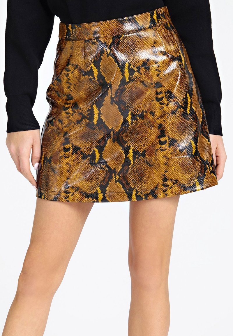 Mini gonna lucida con motivo di pelle di serpente marrone e nera, indossata con una maglietta nera a maniche lunghe, mostrata dalla vita a metà coscia.