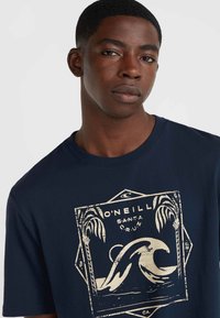 Navy blue cotton t-shirt featuring a cream wave graphic and palm trees within a geometric border. Short sleeves and crew neckline.