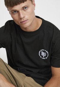 Sort bomulds t-shirt med rund halsudskæring og korte ærmer. Har hvid grafisk tekst og et blomstermotiv på brystet.