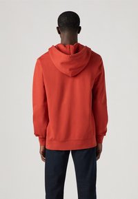 Felpa rossa in cotone con cappuccio regolabile, polsini e bordo a costine. Design semplice, vestibilità comoda, senza motivi o loghi visibili.