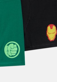 Mustad ja rohelised lühikesed püksid superkangelaste teemaliste trükistega. Roheline osa on rusikasümboliga; mustal osal on punase ja kollase Iron Mani näomask.