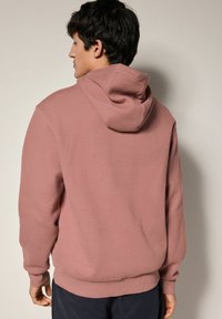 Sudadera rosa texturizada con un patrón en forma de gofre, bolsillo tipo canguro y capucha con cordón. Los puños y la cinturilla acanalados ofrecen un ajuste ceñido.