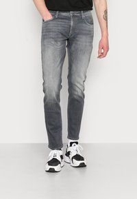 Jeans cinzentos com um corte justo, textura desbotada, design de cinco bolsos e fecho de zíper, combinados com sapatilhas pretas e brancas.