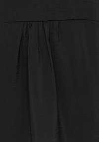 Tissu noir avec des plis verticaux et un détail de couture froncée le long d'une couture horizontale.