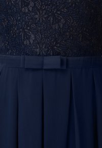 Robe bleu foncé avec un corsage en dentelle texturée et une jupe plissée unie, dotée d'une ceinture en tissu assorti avec un nœud plat à la taille.
